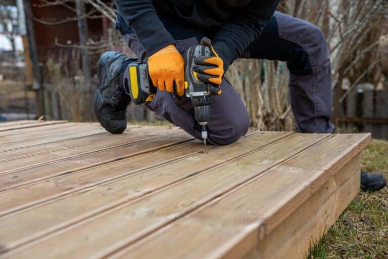 Deck or terrace construction, builder hand with electric screwdriver installing impregnated wooden boards